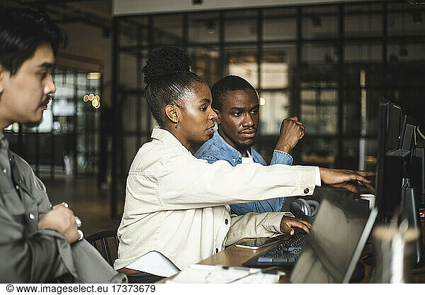Businesswoman discussing with male colleague over computer at startup company