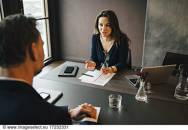 Businesswoman discussing with male colleagues at conference table in office