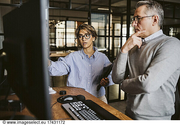Businesswoman discussing with mature male entrepreneur while standing at desk in creative office