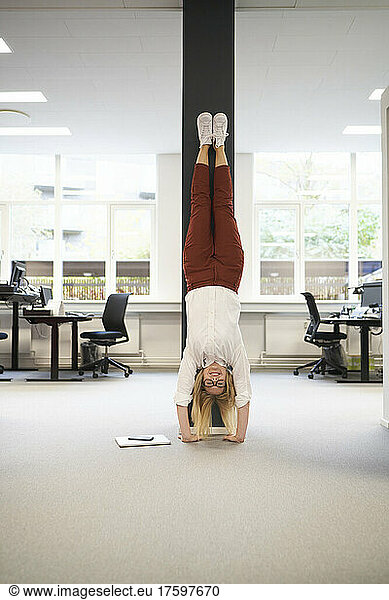 Businesswoman doing handstand in front of a column at office