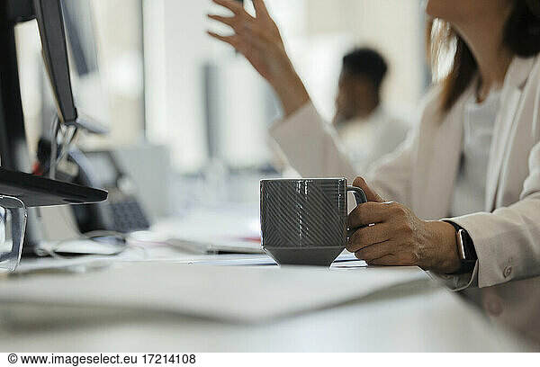 Businesswoman drinking coffee at computer on office desk