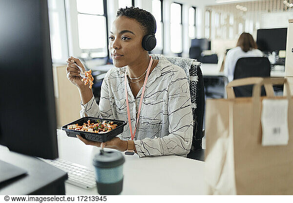 Businesswoman eating takeout lunch at computer in office