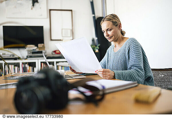 Businesswoman examining photograph sitting with laptop at home
