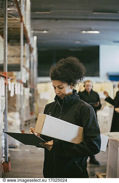 Businesswoman examining while writing on clipboard at distribution warehouse