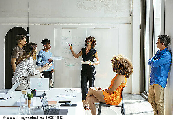 Businesswoman explaining on whiteboard and having discussion with colleagues