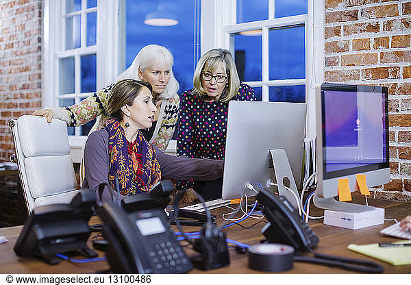 Businesswoman explaining to female colleagues through desktop computer at desk