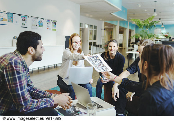 Businesswoman giving photographs to colleague during meeting in creative office