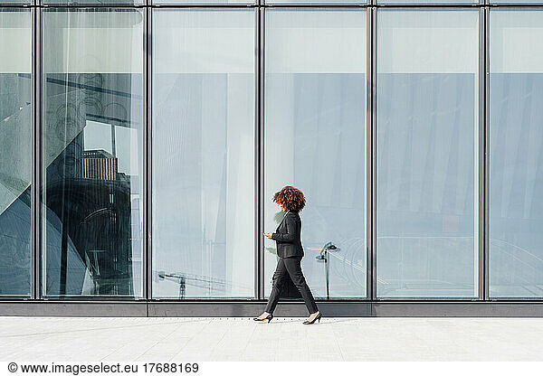 Businesswoman holding bag walking by glass wall