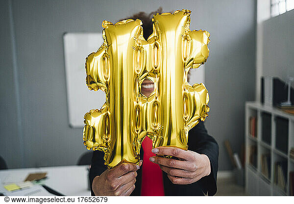 Businesswoman holding golden hashtag symbol balloon in front of face