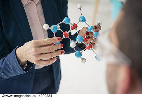 Businesswoman holding molecule model teaching teenage boy