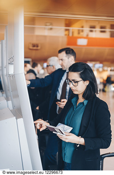 Businesswoman holding passport while using automated check-in machine in airport