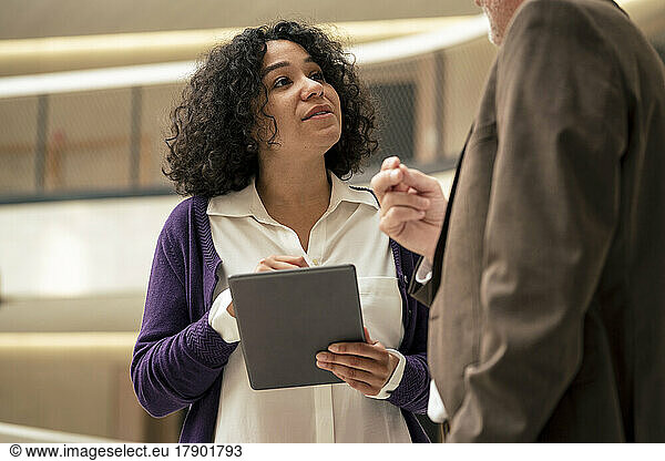 Businesswoman holding tablet PC discussing ideas with colleague in corridor
