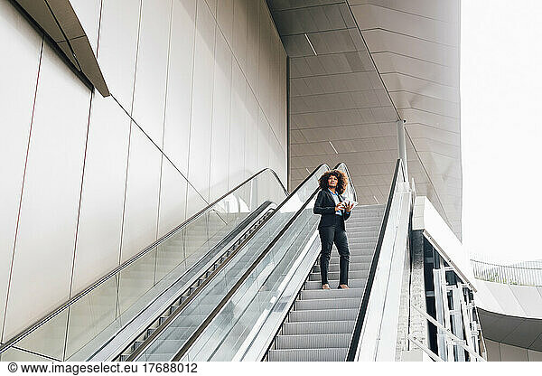 Businesswoman holding tablet PC standing on escalator
