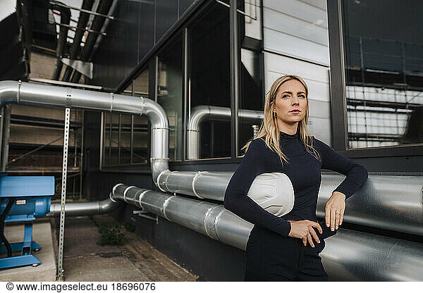 Businesswoman leaning on metal pipes at factory