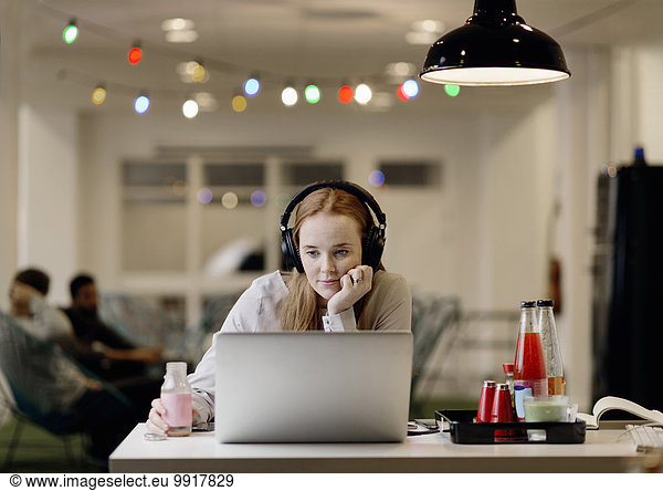 Businesswoman listening music while working late on laptop in creative office