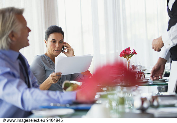 Businesswoman looking at chart and talking on mobile phone at restaurant table