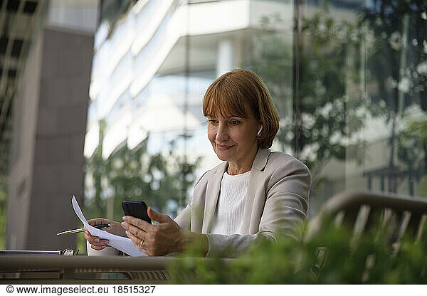 Businesswoman looking at smart phone sitting at sidewalk cafe