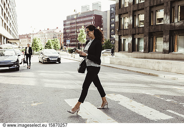 Businesswoman looking at smart phone while crossing street