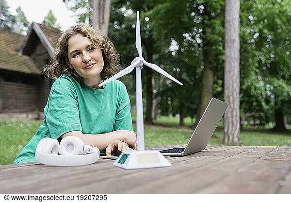 Businesswoman looking at wind turbine model with wireless technologies on table in forest