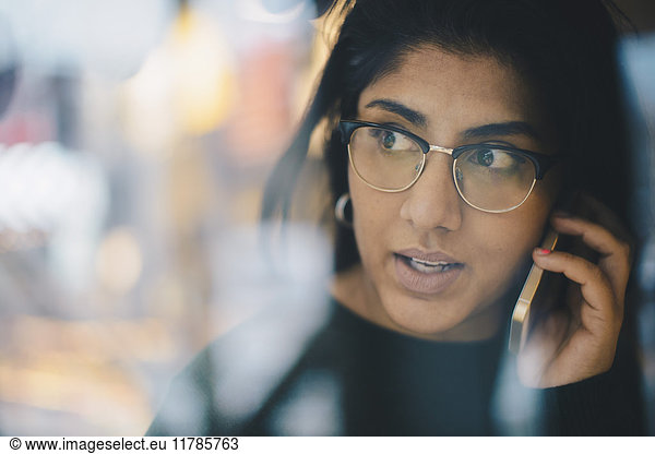 Businesswoman looking away while using smart phone seen through glass