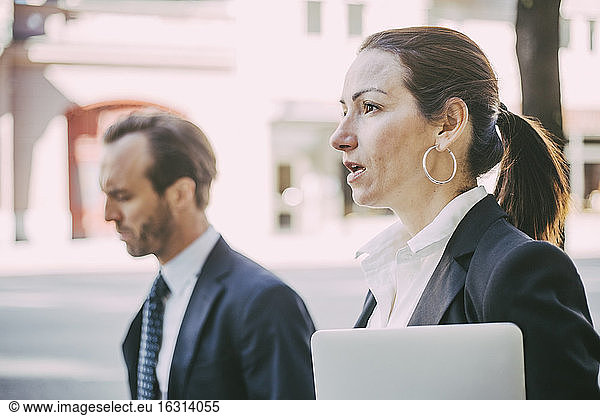 Businesswoman looking away while walking with coworker in city