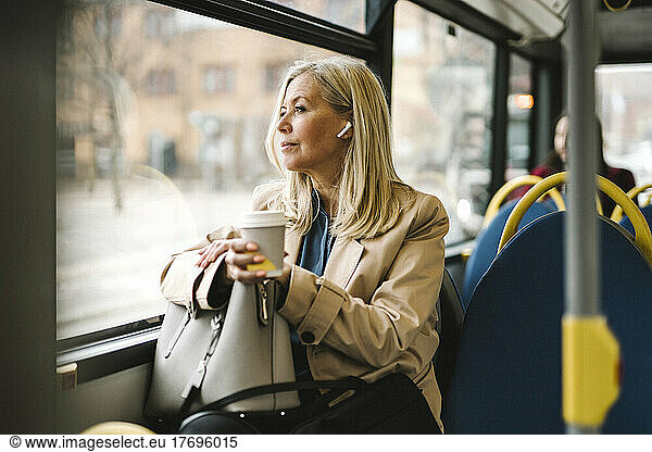 Businesswoman looking through window holding disposable cup while commuting in bus