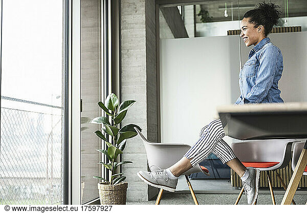 Businesswoman looking through window sitting at work place