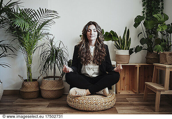 Businesswoman meditating by plants in office