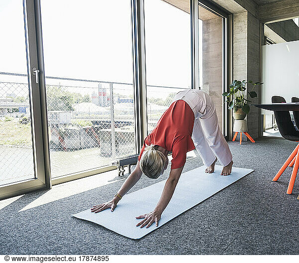 Businesswoman practicing Adho Mukha Svanasana on exercise mat in office