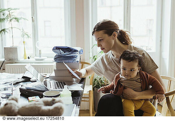 Businesswoman reading document while sitting with baby boy in living room