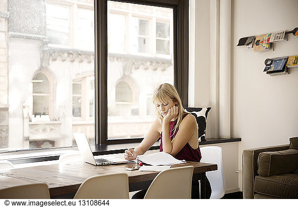 Businesswoman reading file at desk by window in creative office