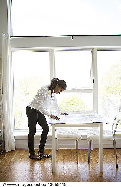 Businesswoman reading map at table against windows in creative office