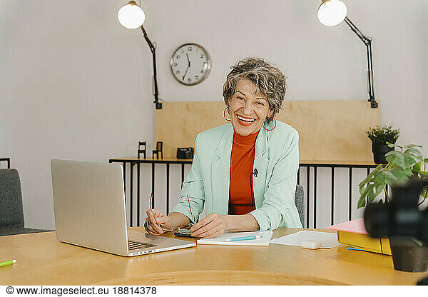 Businesswoman recording online class sitting at table in studio