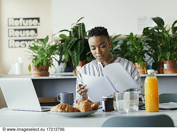 Businesswoman reviewing paperwork at breakfast in office lounge