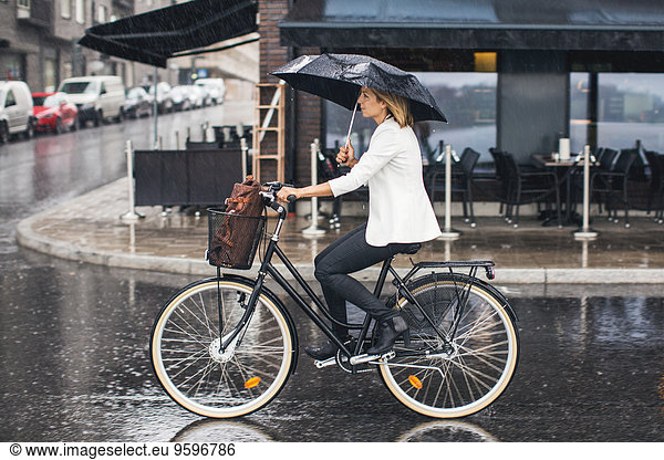 Businesswoman riding bicycle on wet city street during rainy season