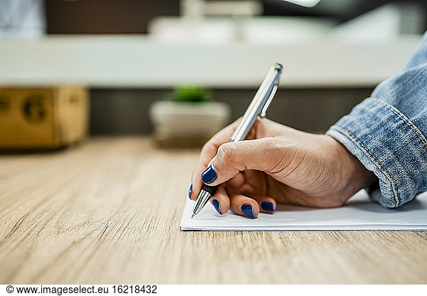 Businesswoman's hand writing on document at wooden desk in modern office