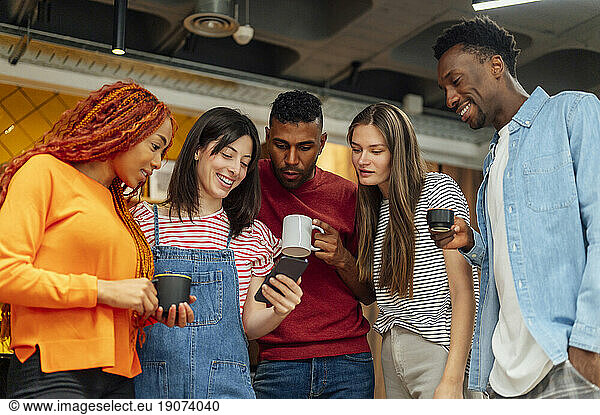 Businesswoman sharing smart phone with colleagues having coffee at office