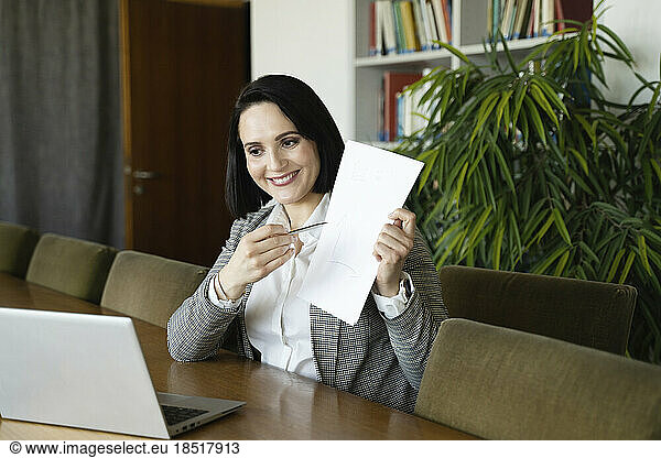 Businesswoman showing document on video call through laptop at office