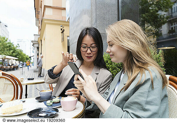 Businesswoman showing over smart phone to partner at sidewalk cafe
