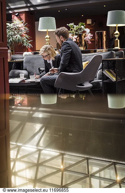 Businesswoman signing agreement by male partner sitting in hotel reception