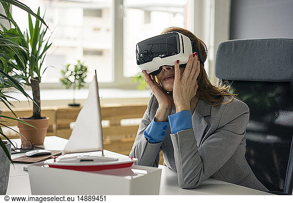 Businesswoman sitting at desk with a ship model  looking through VR glasses