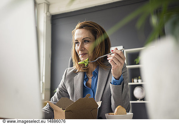 Businesswoman sitting in office  working on PC  eating lunch