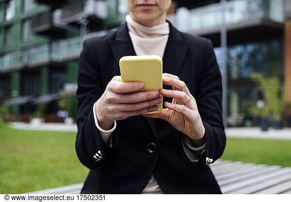 Businesswoman sitting on office park bench using mobile phone