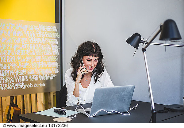 Businesswoman smiling while talking on mobile phone at desk in creative office