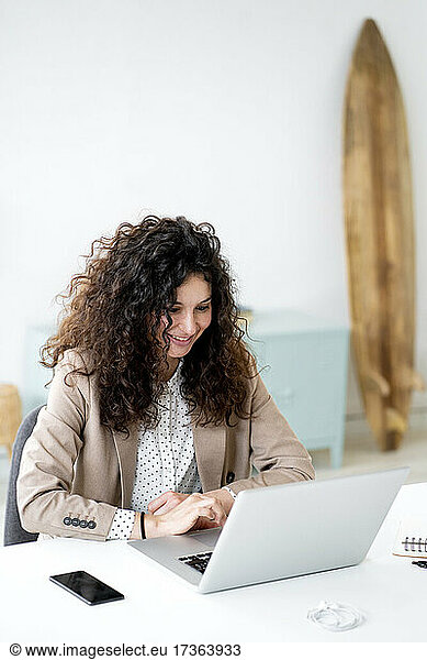 Businesswoman smiling while using laptop at desk in office