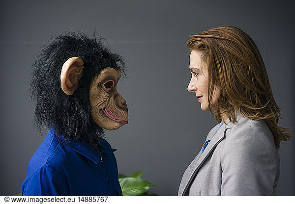 Businesswoman standing face to face with a trainee  wearing monkey mask and blue oevrall