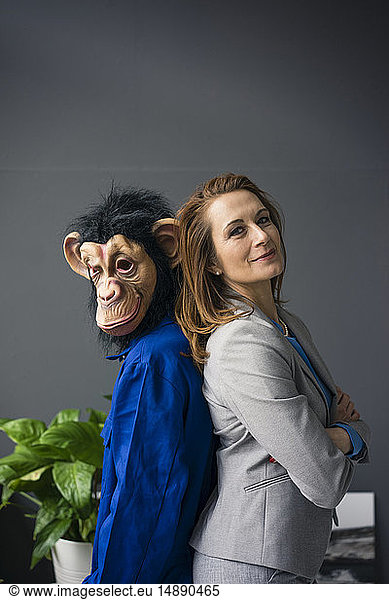 Businesswoman standing fback to back with a trainee  wearing monkey mask and blue oevrall