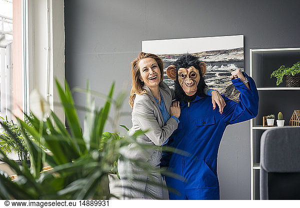 Businesswoman standing in office with a trainee  wearing monkey mask and blue oevrall