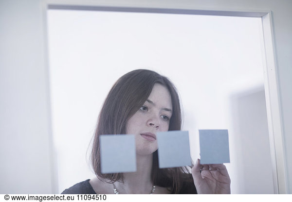 Businesswoman sticking adhesive notes on glass