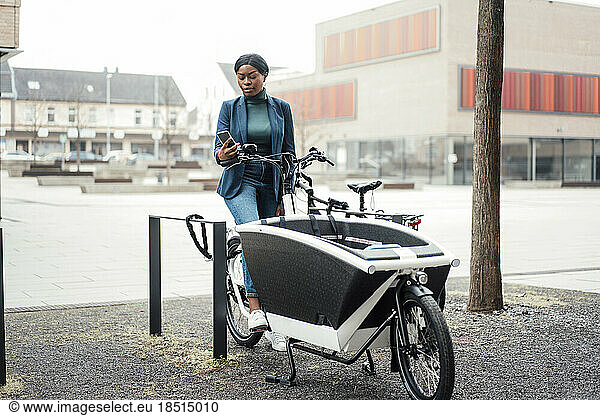 Businesswoman surfing net through smart phone sitting on cargo bike